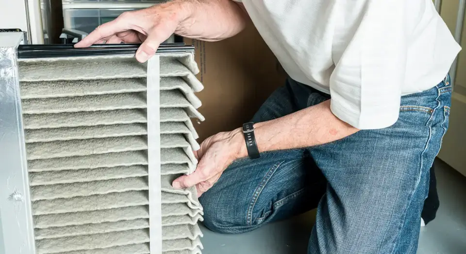 A man checks his HVAC air filter, finds it to be very dirty and clogged.