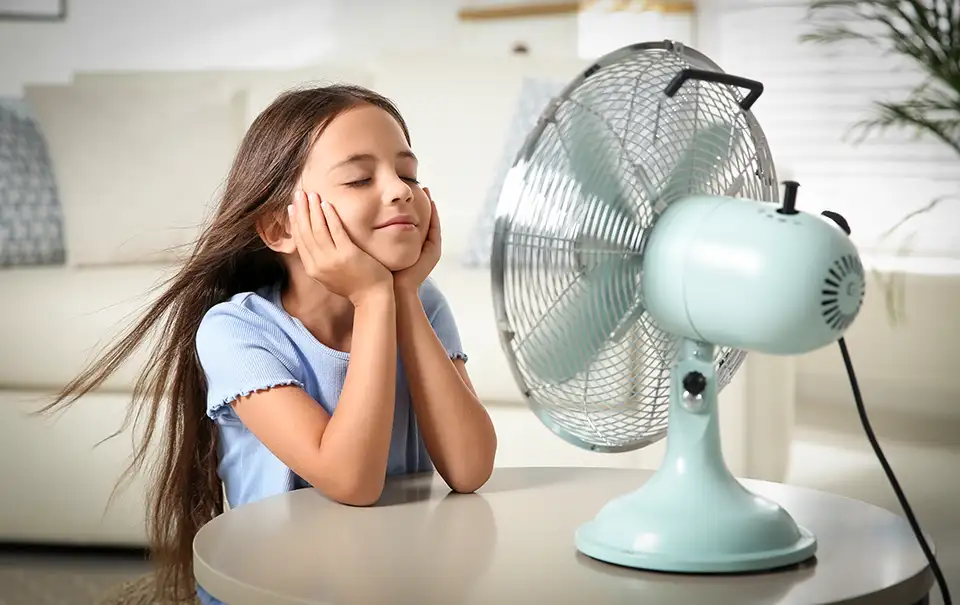 A young girl sits in front of an fan, enjoying the cool breeze.