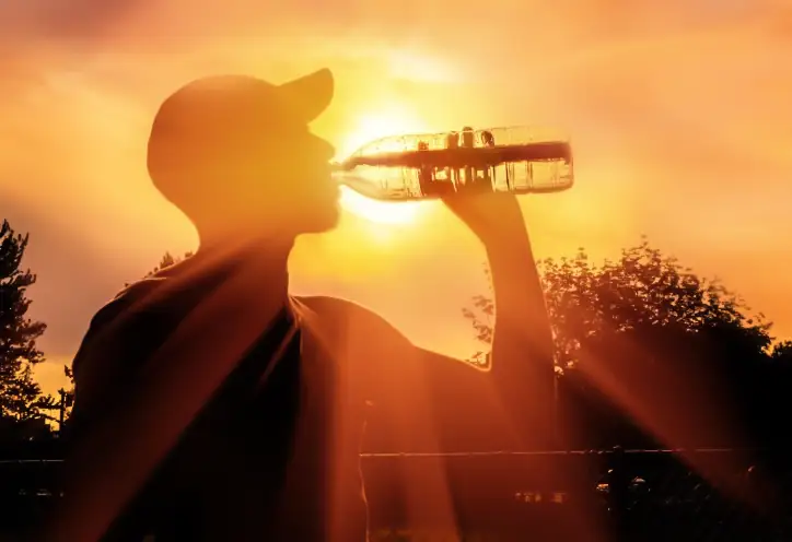 Man drinks bottle of water as the sweltering sun sets behind him.