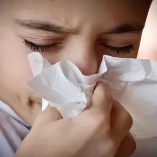 Little boy suffering from allergies blows his nose with a tissue.