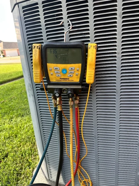 Fieldpiece digital manifold gauge attached to outdoor AC unit showing refrigerant pressure readings during system evacuation and recharge