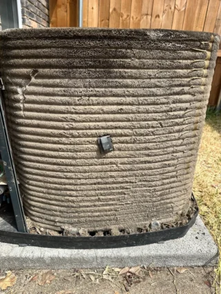 Heavily soiled AC condenser unit with dirt and debris buildup covering the horizontal fins and coils