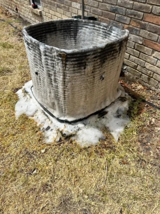 Dirty AC condenser unit with heavy buildup of dust and debris against brick foundation in Mesquite area