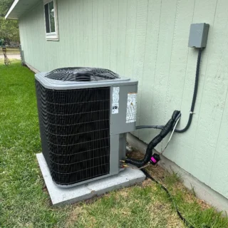 New R454B heat pump system installed outside light green house with conduit running to outdoor unit mounted on concrete pad