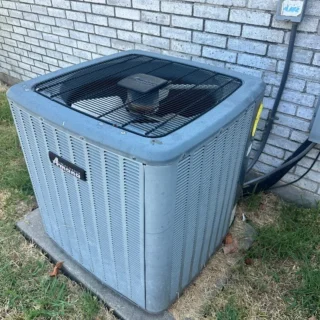 Dirty air conditioning condenser unit mounted against brick wall in Mesquite residential yard