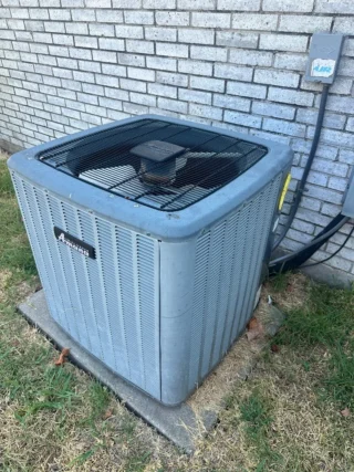 Dirty air conditioning condenser unit mounted against brick wall in Mesquite residential yard