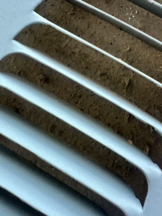 Clogged HVAC condenser coil with dirt and debris buildup between white fins, showing restricted airflow