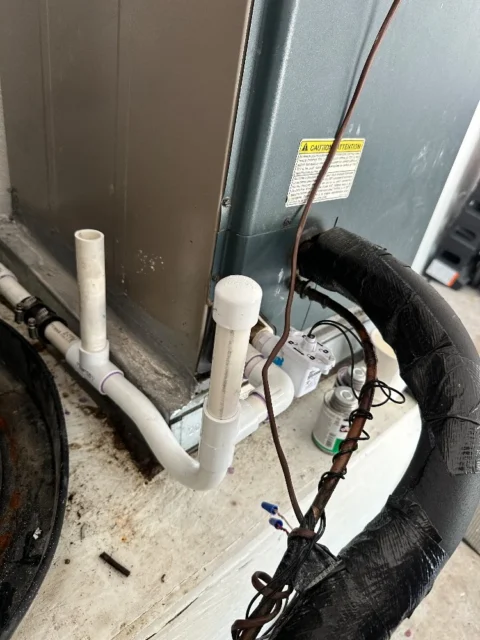 AC drain pan with float switch and white PVC condensate lines, inspected during Garland service call