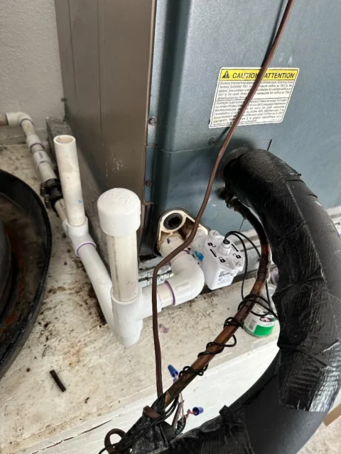 Secondary drain pan with float switch and white PVC pipes beneath HVAC unit during Garland service call