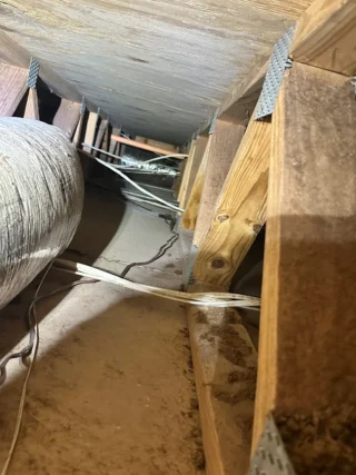 HVAC condensation drain hose rerouted and secured with metal strapping in crawl space during installation repair