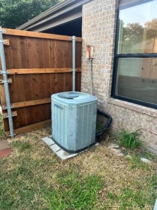 New air conditioning unit installed on concrete pad beside brick home in Mesquite, TX