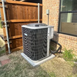 Newly installed air conditioning unit on concrete pad against brick home exterior in Mesquite, TX