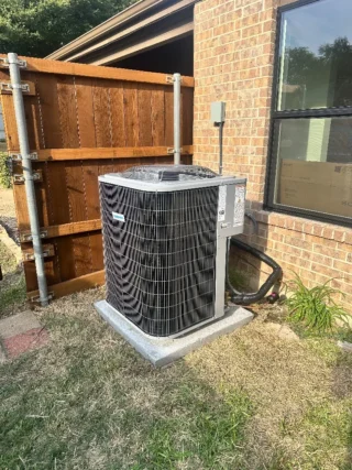 Newly installed air conditioning unit on concrete pad against brick home exterior in Mesquite, TX