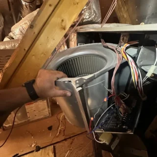 Technician's hand installing a replacement blower fan motor into an HVAC unit during warranty service repair in Mesquite area.