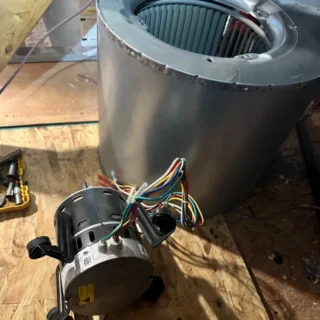 Replacement blower fan motor with colorful wiring harness positioned below its silver housing during HVAC repair installation.