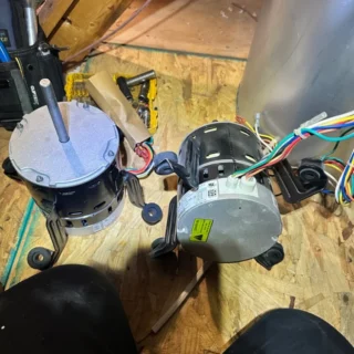 Two HVAC blower fan motors on wooden workbench with colorful wiring and mounting brackets visible.