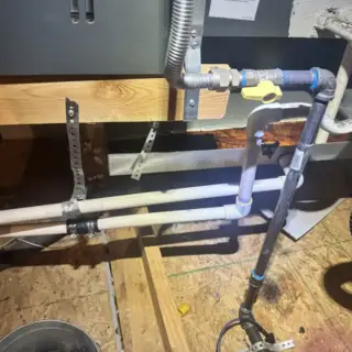 HVAC technician clearing a clogged drain line with vacuum equipment and blue tape-wrapped pipes in Garland home