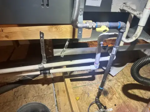 HVAC technician clearing a clogged drain line with vacuum equipment and blue tape-wrapped pipes in Garland home